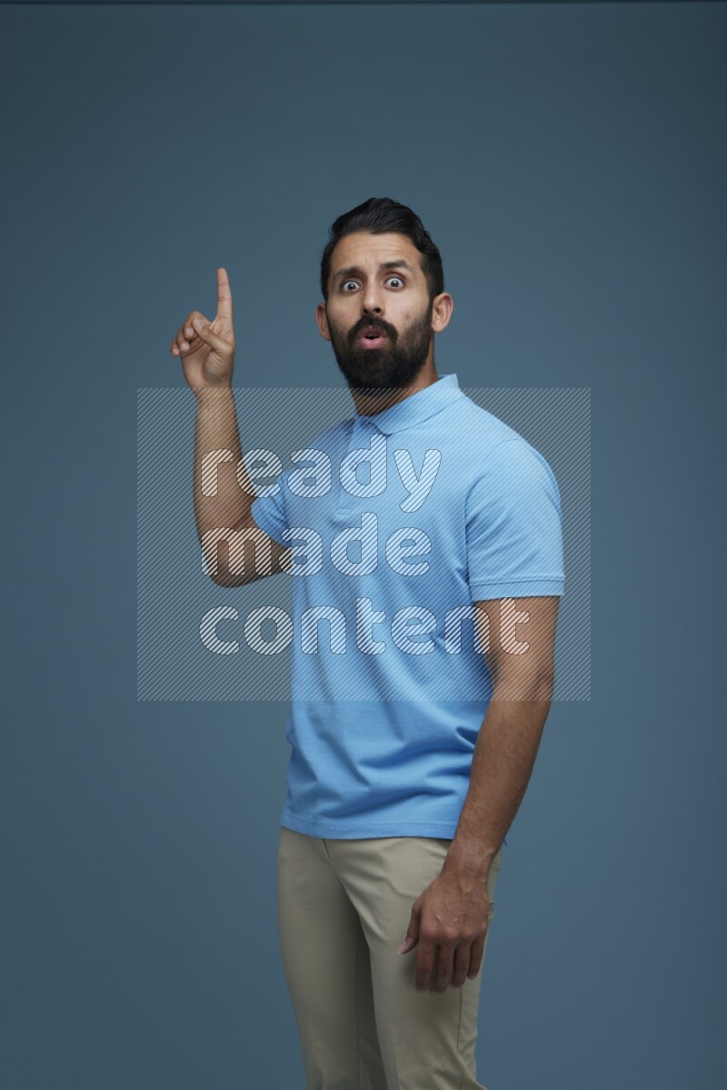 A man pointing  in a blue background wearing a Blue shirt