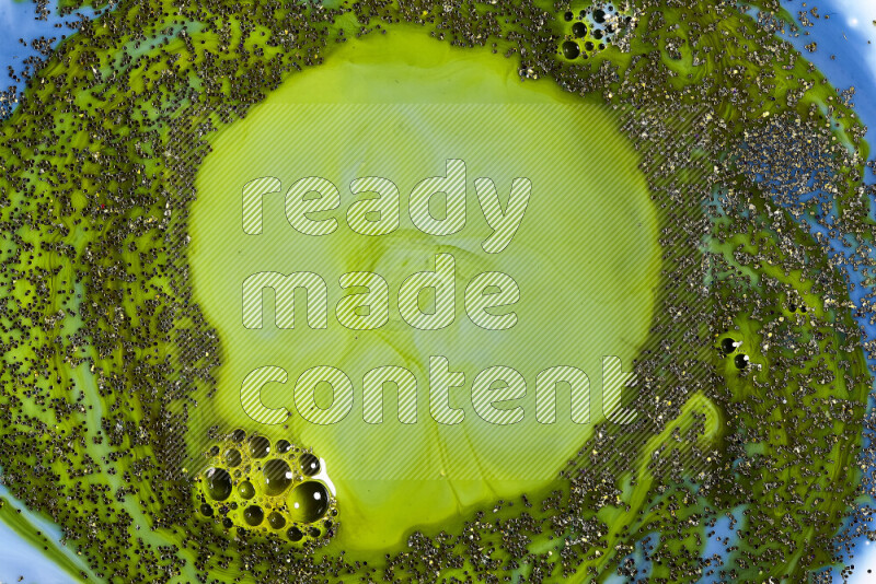 A close-up of sparkling gold glitter scattered on swirling blue and green background