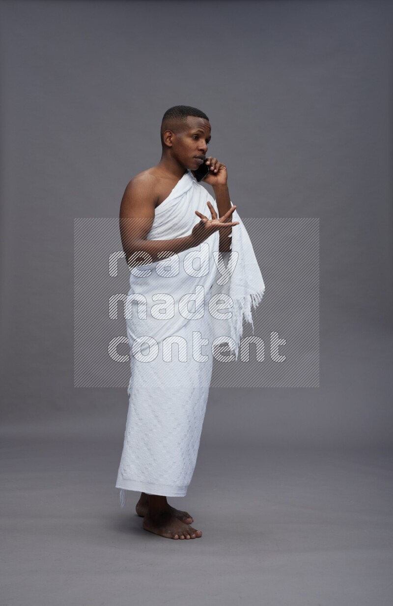 A man wearing Ehram Standing talking on phone on gray background
