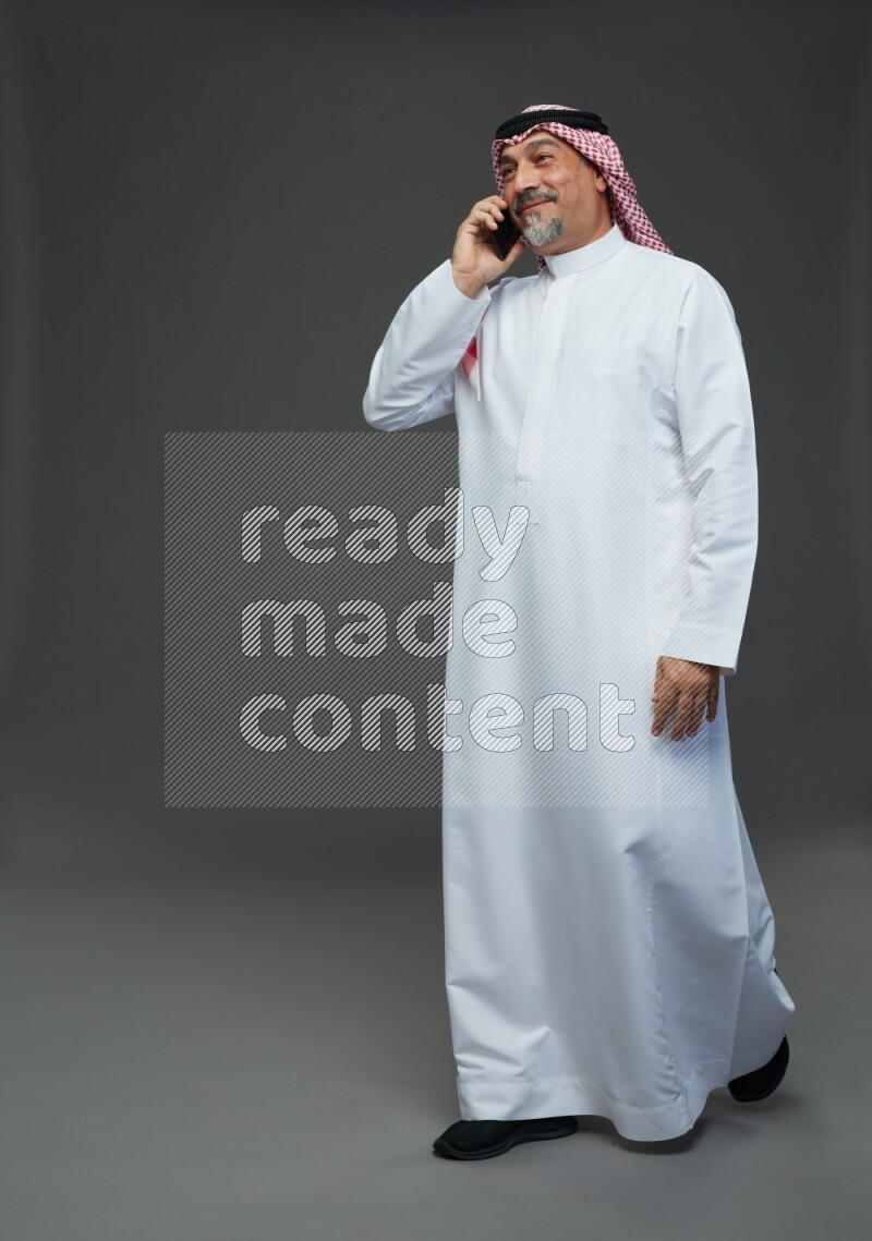 Saudi man with shomag Standing talking on phone on gray background