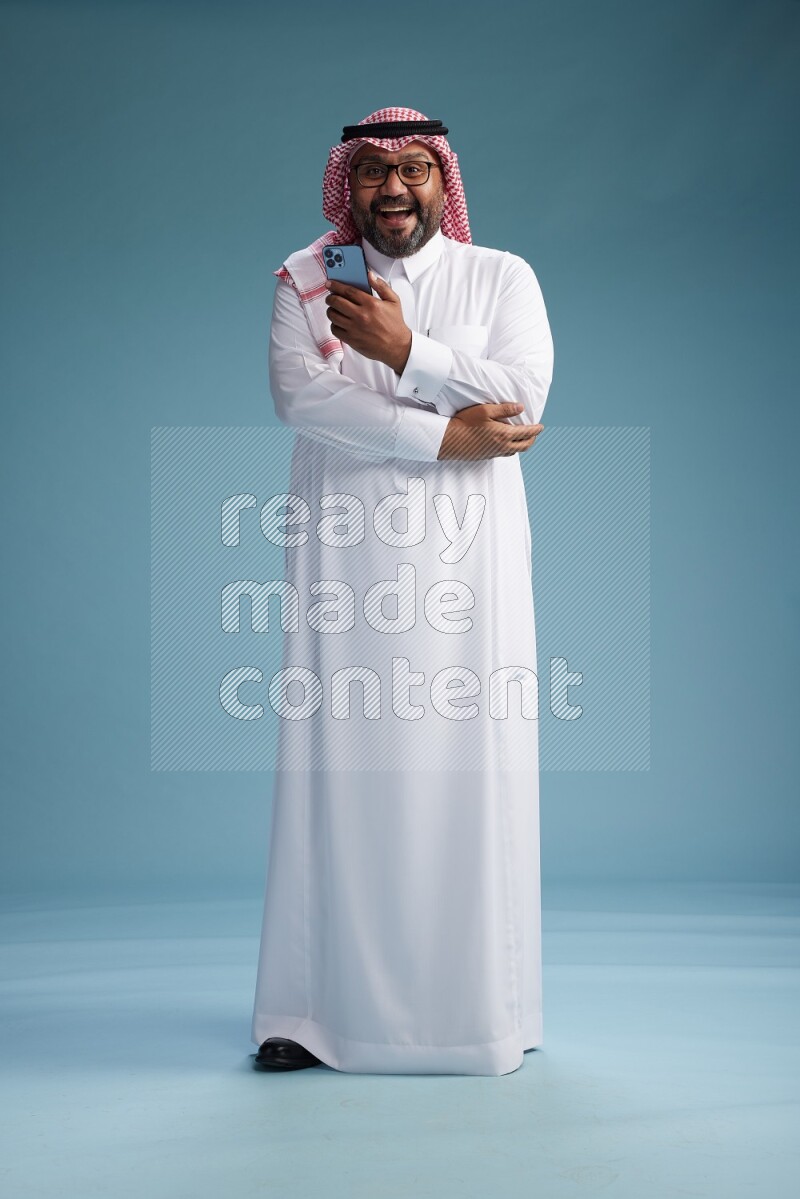 Saudi Man with shimag Standing texting on phone on blue background