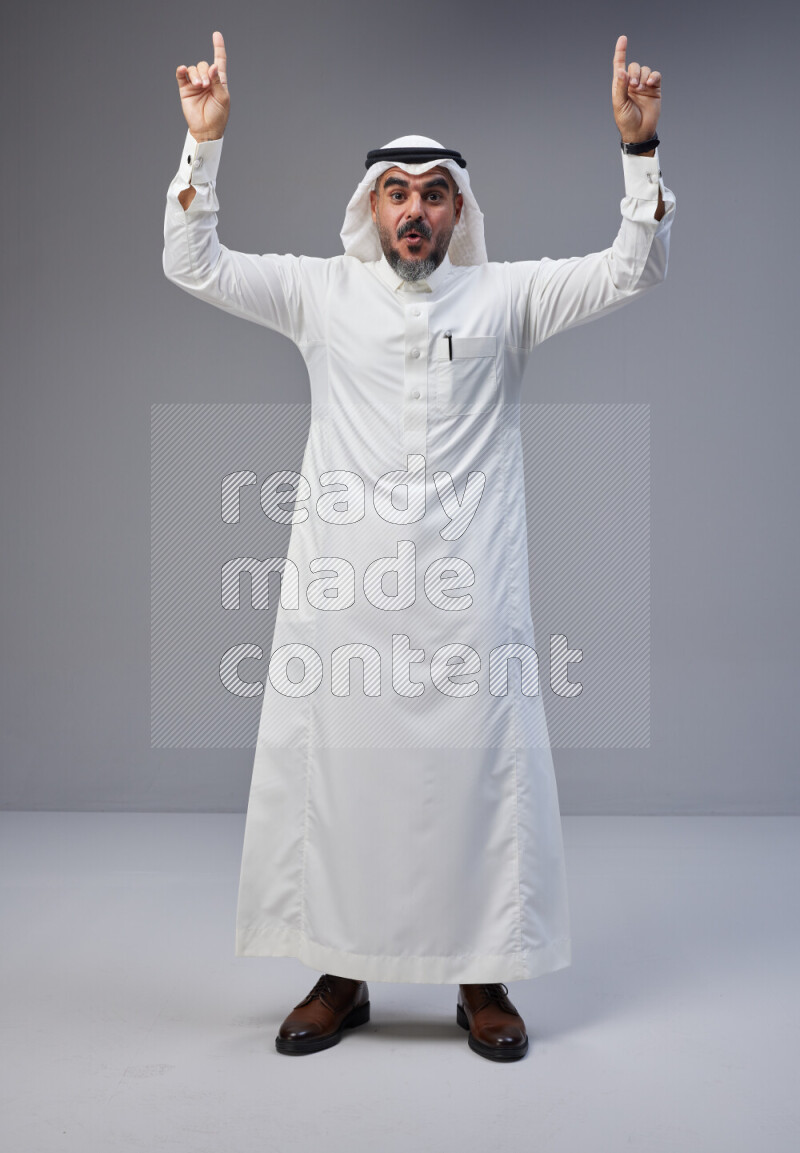Saudi man Wearing Thob and white Shomag standing interacting with the camera on Gray background