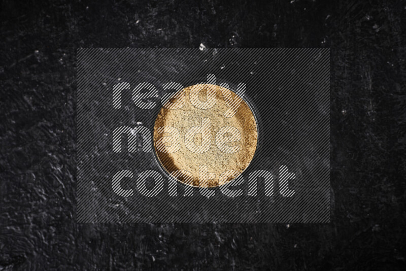 A black pottery bowl full of ground ginger powder on black background