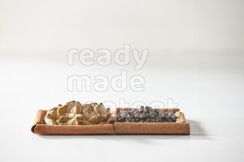 2 squares of cinnamon sticks full of black peppers and turmeric fingers on white flooring