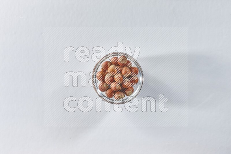 A glass bowl full of hazelnuts on a white background in different angles