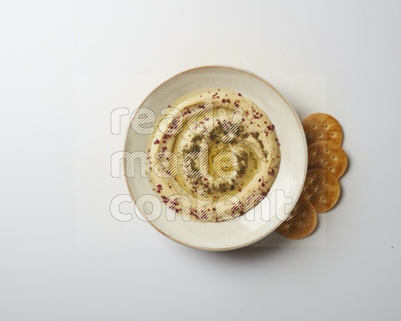 Hummus in a pottry plate garnished with zaatr & sumak on a white background