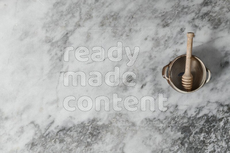 Multicolored pottery bowl with wooden honey dipper in it on grey marble background