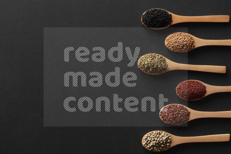 الفلفل الأسود وحبوب الخردل وحبة البركة وحب الرشاد والكمون و حبوب الكتان في معالق خشبية علي خلفية سوداء