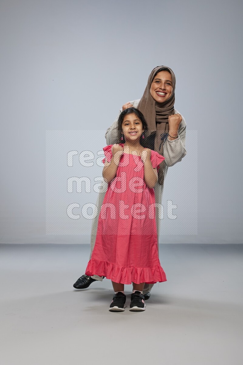A girl and her mother interacting with the camera on gray background