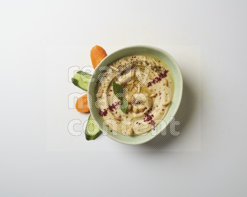 Hummus in a green plate garnished with zattar & sumak on a white background