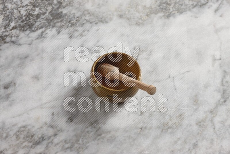 وعاء فخاري متعدد الألوان مع ملعقة عسل خشبية بداخله على خلفية من الرخام الرمادي