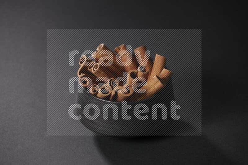 Cinnamon sticks in a black bowl on a black background in different angles