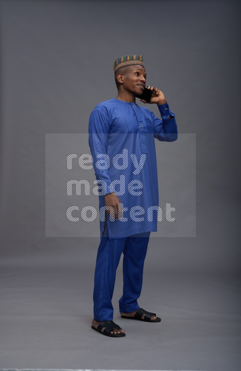 Man wearing Nigerian outfit standing talking on phone on gray background