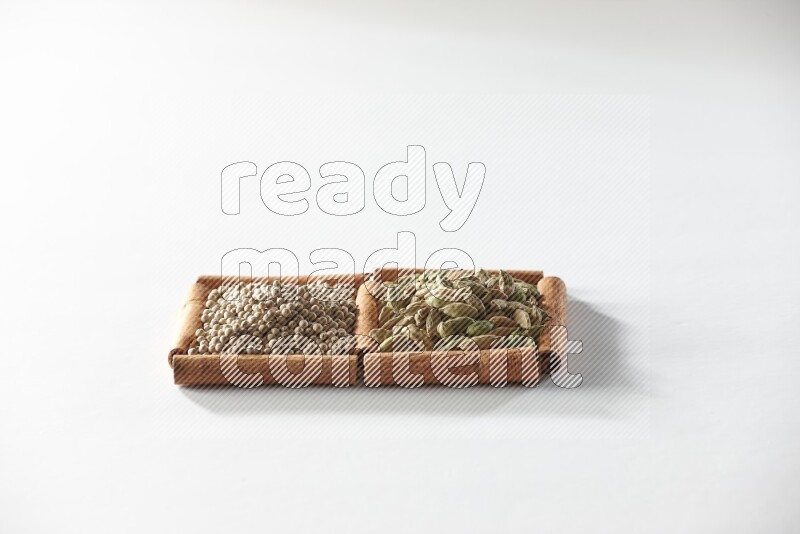 مربعان من أعواد القرفة ممتلئان بحبوب الهيل وحبوب الفلفل الأبيض علي خلفية بيضاء