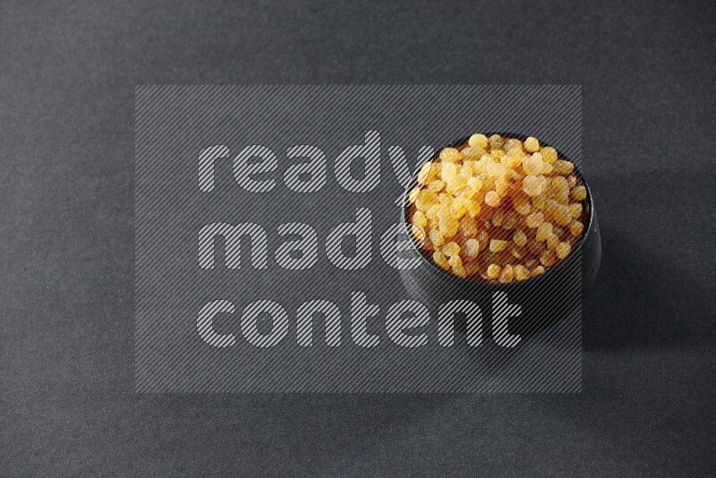 وعاء فخاري أسود ممتلئ بالزبيب الأصفر على خلفية سوداء