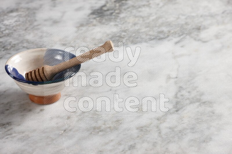 Multicolored pottery bowl with wooden honey dipper in it on grey marble background