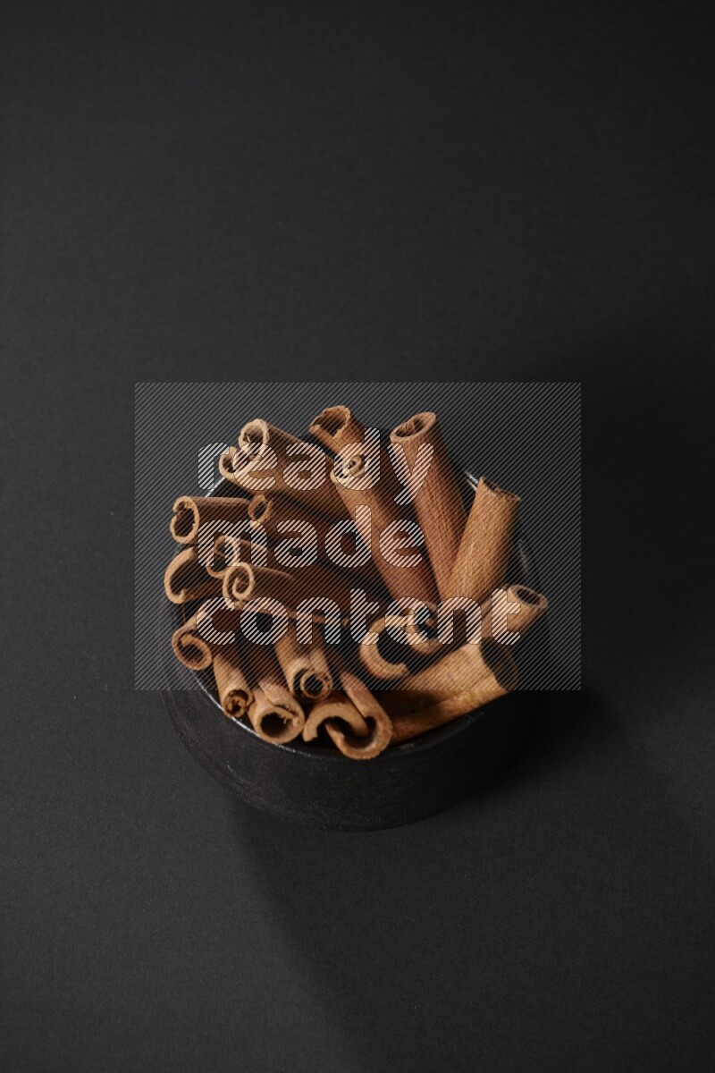Cinnamon sticks in a black bowl on a black background in different angles
