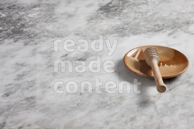 طبق فخاري متعدد الألوان مع ملعقة عسل خشبية بداخله على خلفية من الرخام الرمادي