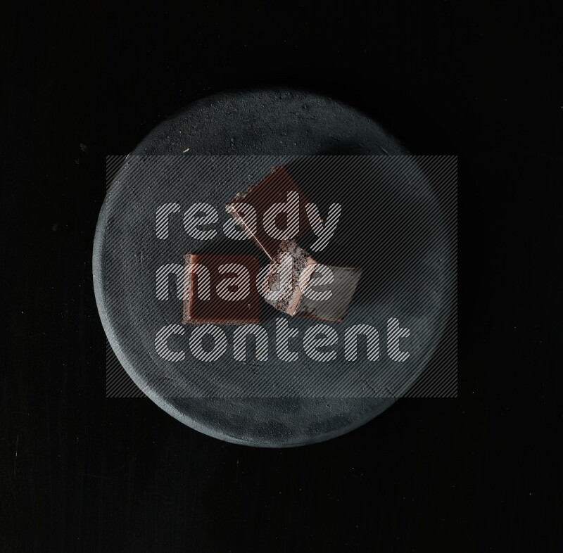 Assorted desserts in a black pottery plate on black background