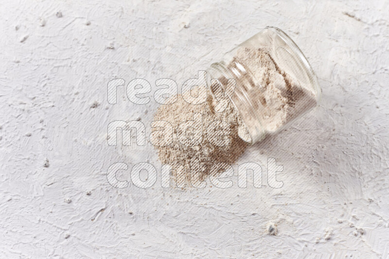 A glass jar full of onion powder flipped with some spilling powder on white background