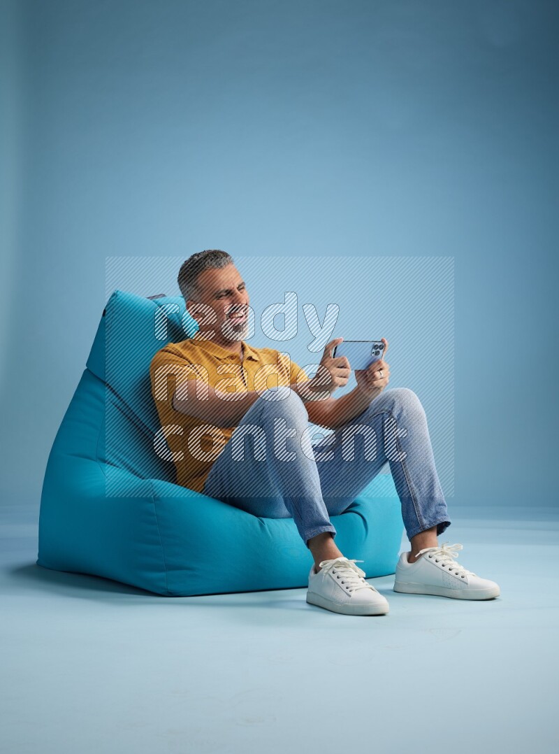A man sitting on a blue beanbag and playing on phone