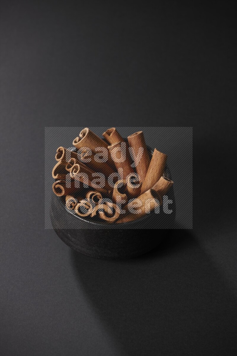Cinnamon sticks in a black bowl on a black background in different angles