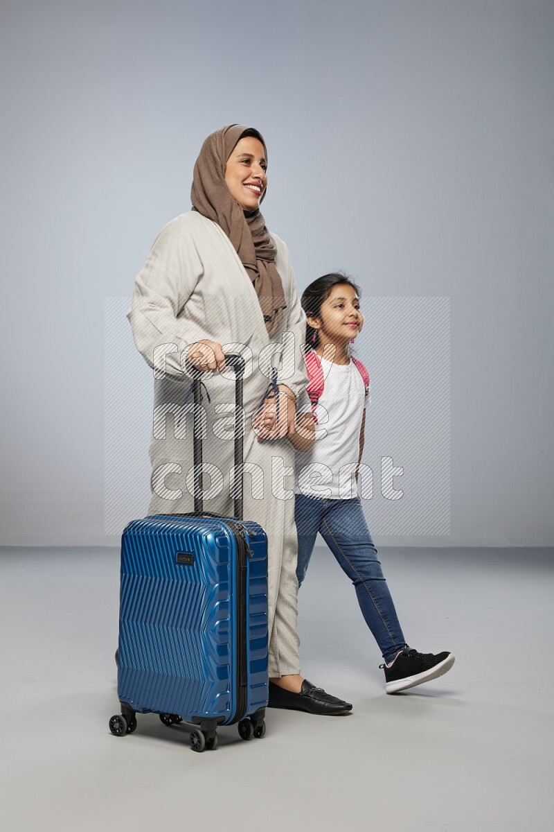Mom and daughter standing pulling a carry-on bag on gray background