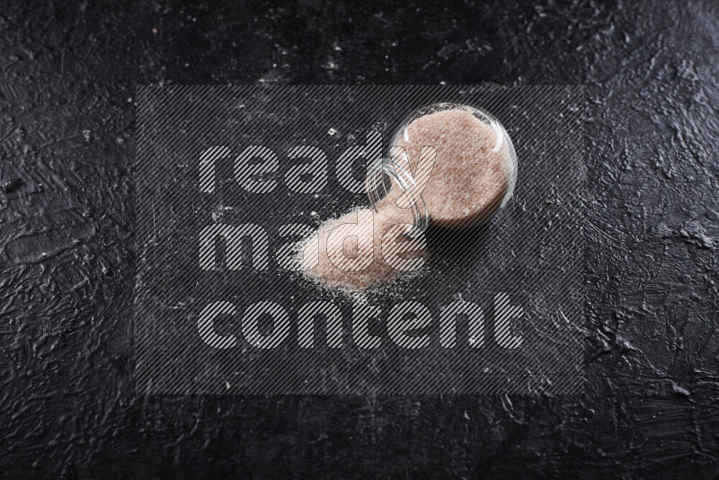 A glass jar full of fine himalayan salt on black background