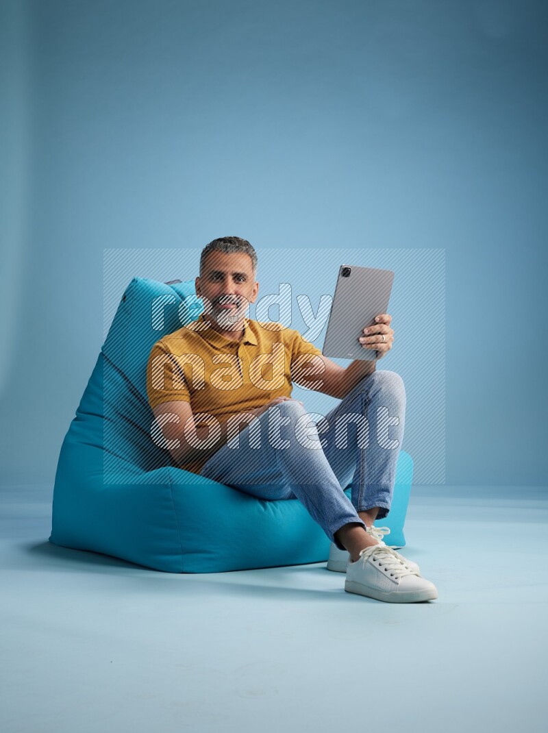 A man sitting on a blue beanbag and working on tablet