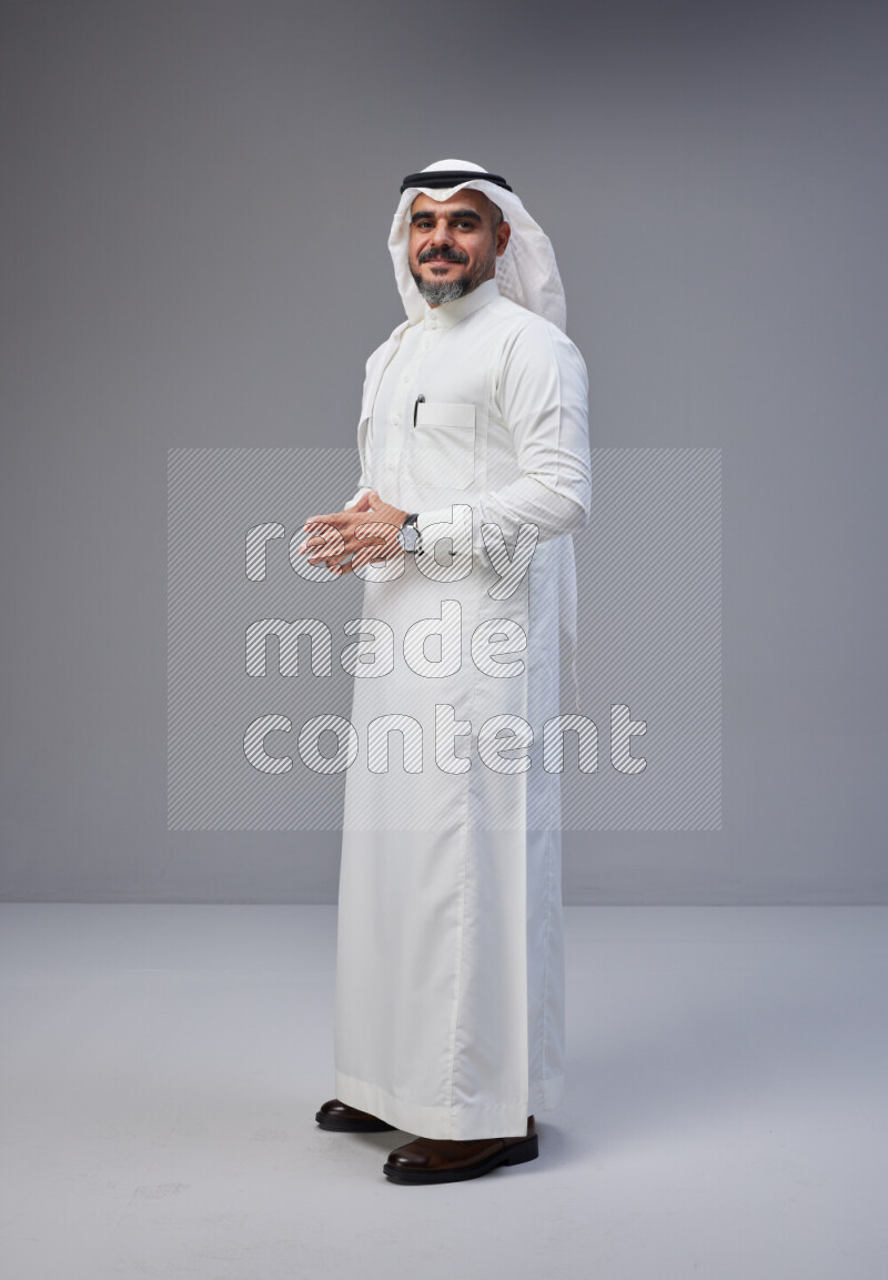 Saudi man Wearing Thob and white Shomag standing interacting with the camera on Gray background