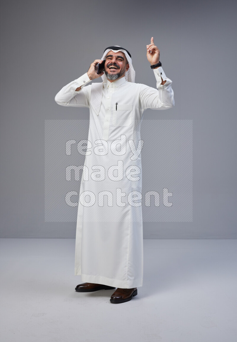 Saudi man Wearing Thob and white Shomag standing talking on phone on Gray background
