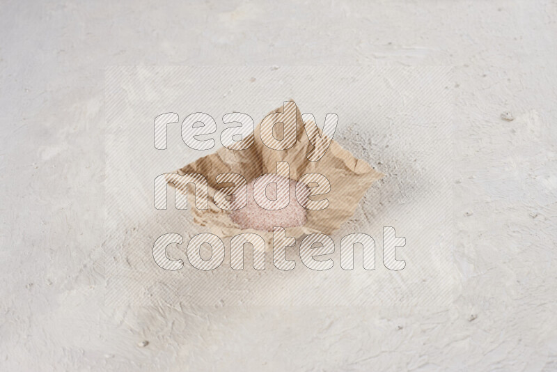 A crumpled piece of paper full of pink himalayan salt on white background