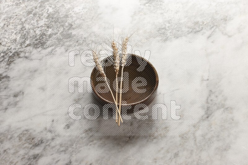 Wheat stalks on multicolored pottery oven plate on grey marble background