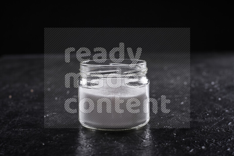 A glass jar full of fine table salt on black background