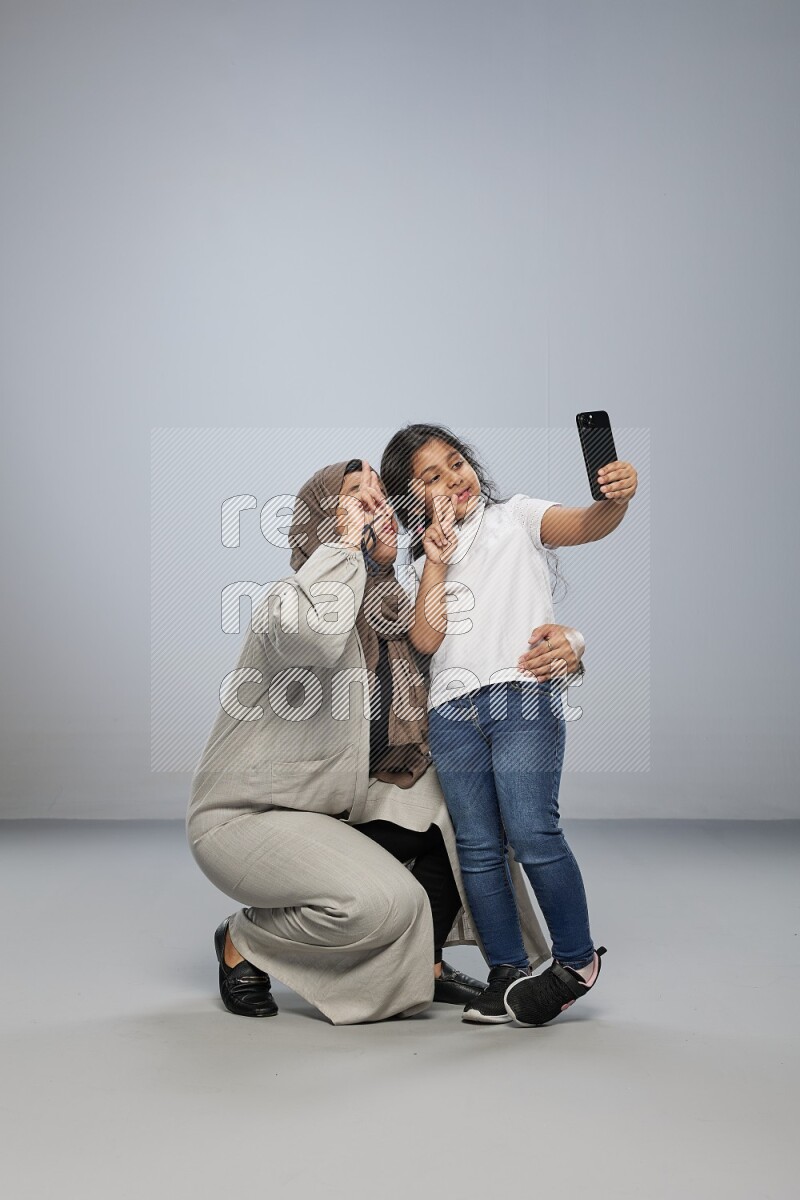 A girl standing taking selfie with her mother on gray background