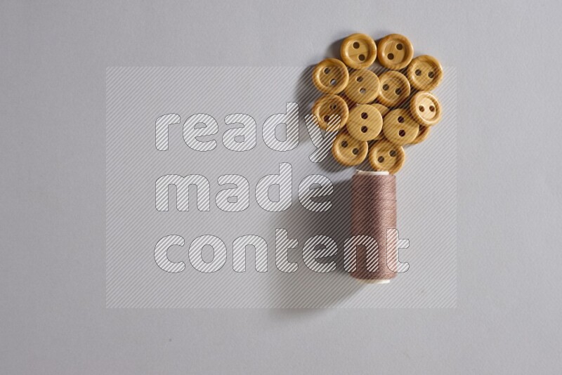 A brown sewing thread spool with colored buttons on grey background
