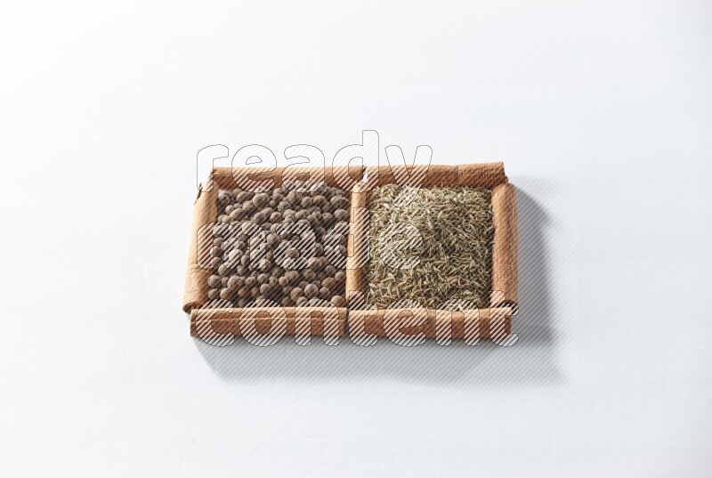 مربعان من أعواد القرفة ممتلئان ببهار الفلفل الحلو والكمون علي خلفية بيضاء