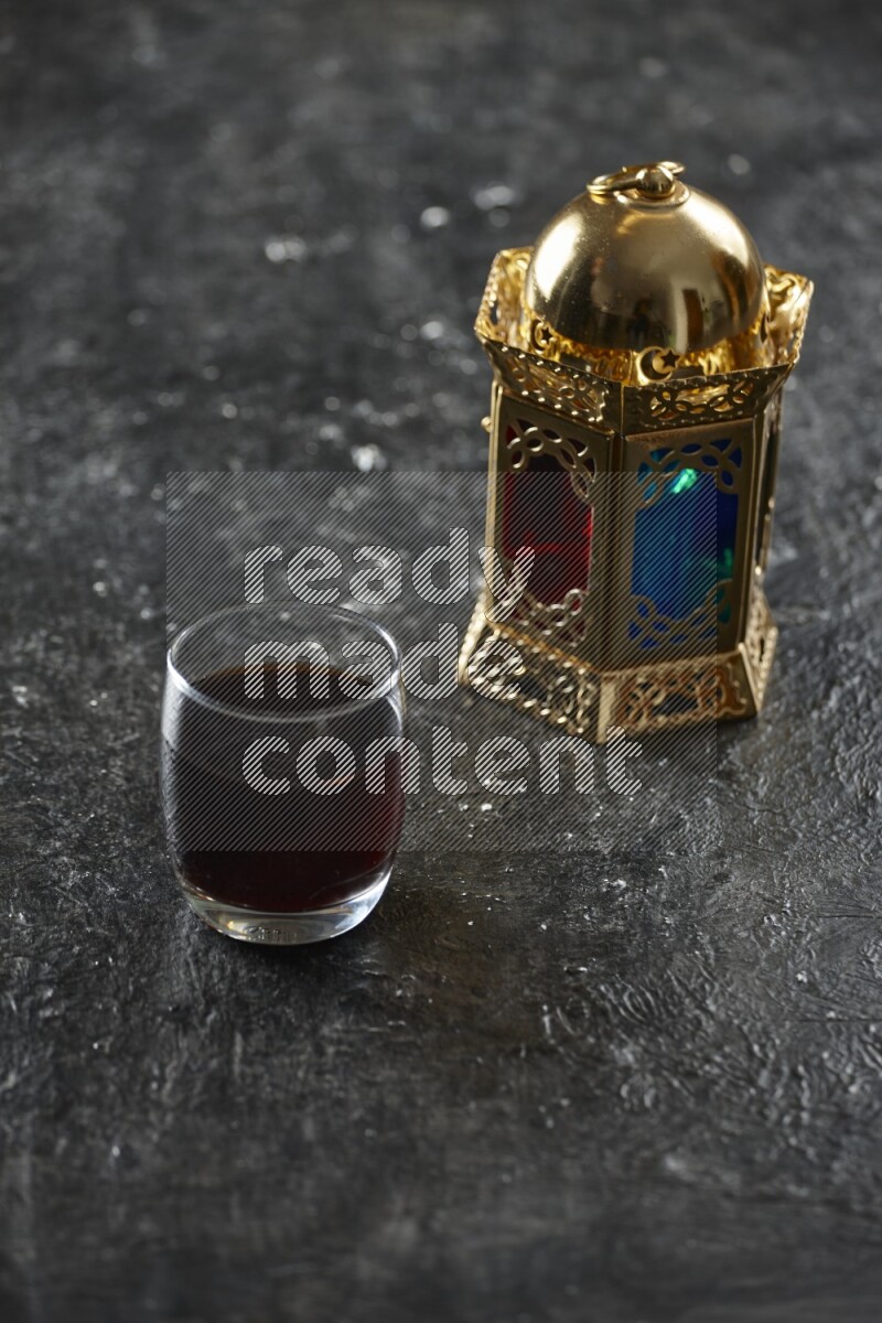 A golden lantern with different drinks, dates, nuts, prayer beads and quran on textured black background