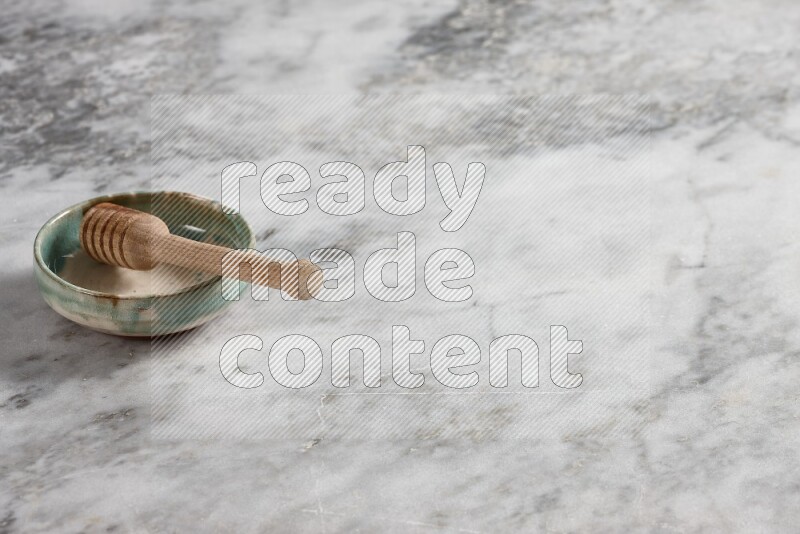 Multicolored pottery bowl with wooden honey dipper in it on grey marble background