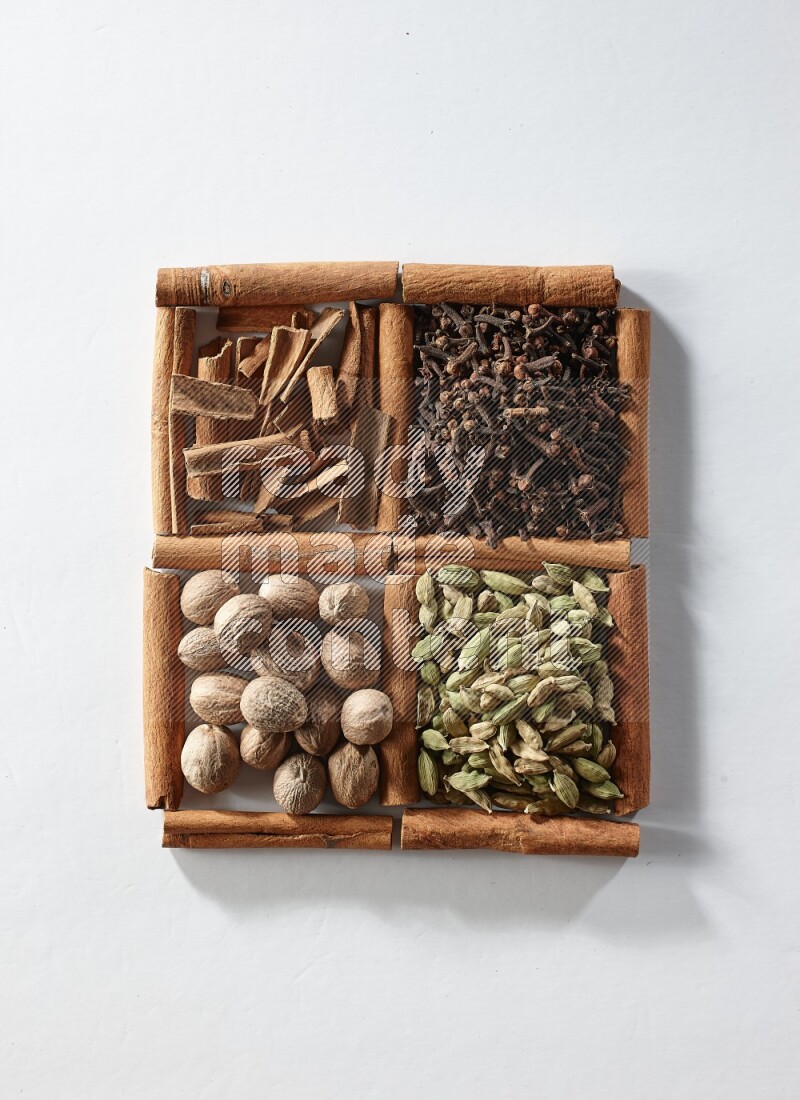 4 مربعات من أعواد القرفة ممتلئة بالهيل والقرفة والقرنفل وجوزة الطيب على أرضية بيضاء
