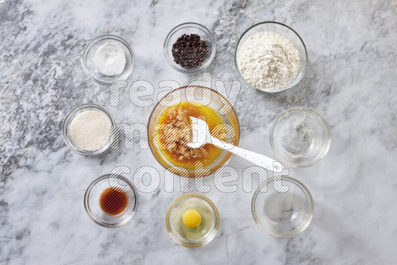 كوكيز خطوة بخطوة بمكوناتها، الدقيق، الزبدة، السكر البني، البيض، الفانيليا، السكر الأبيض، رقائق الشوكولاتة وصودا الخبز على خلفية رخام رمادي