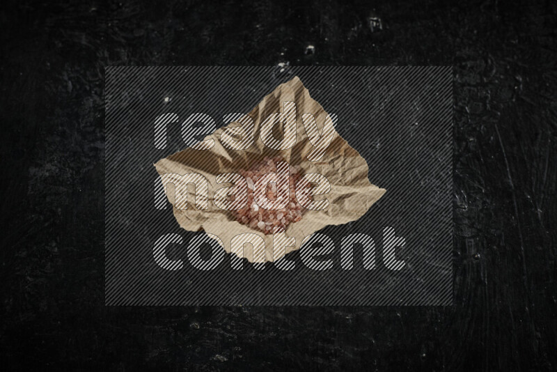 A crumpled piece of paper full of pink himalayan salt on black background