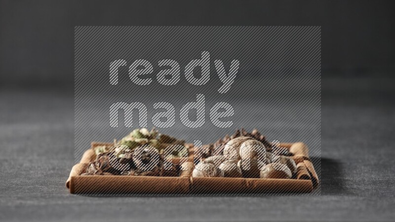 4 مربعات من عيدان القرفة ممتلئة بحب الهيل واليانسون النجمي وجوزة الطيب والقرنفل على أرضية سوداء