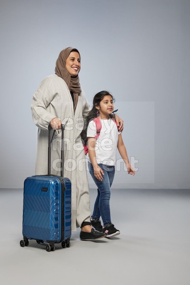 Mom and daughter standing pulling a carry-on bag on gray background