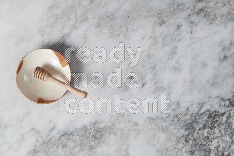 طبق فخاري متعدد الألوان مع ملعقة عسل خشبية بداخله على خلفية من الرخام الرمادي