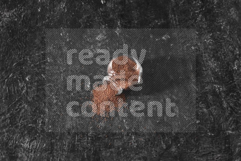 وعاء زجاجي مقلوب ممتلئ ببذور حب الرشاد وتناثرت البذور منه على أرضية سوداء