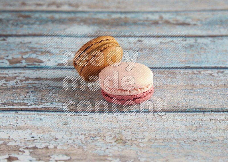 45º Shot of of two assorted Brown Irish Cream, and Pink Litchi Raspberry macarons on light blue background