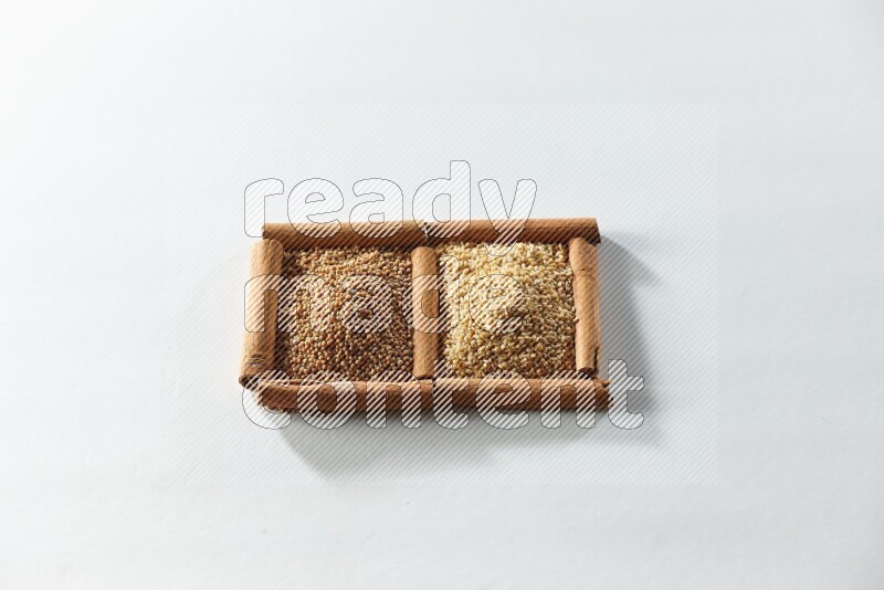 مربعان من أعواد القرفة ممتلئان بحبوب الخردل وبذور السمسم علي خلفية بيضاء