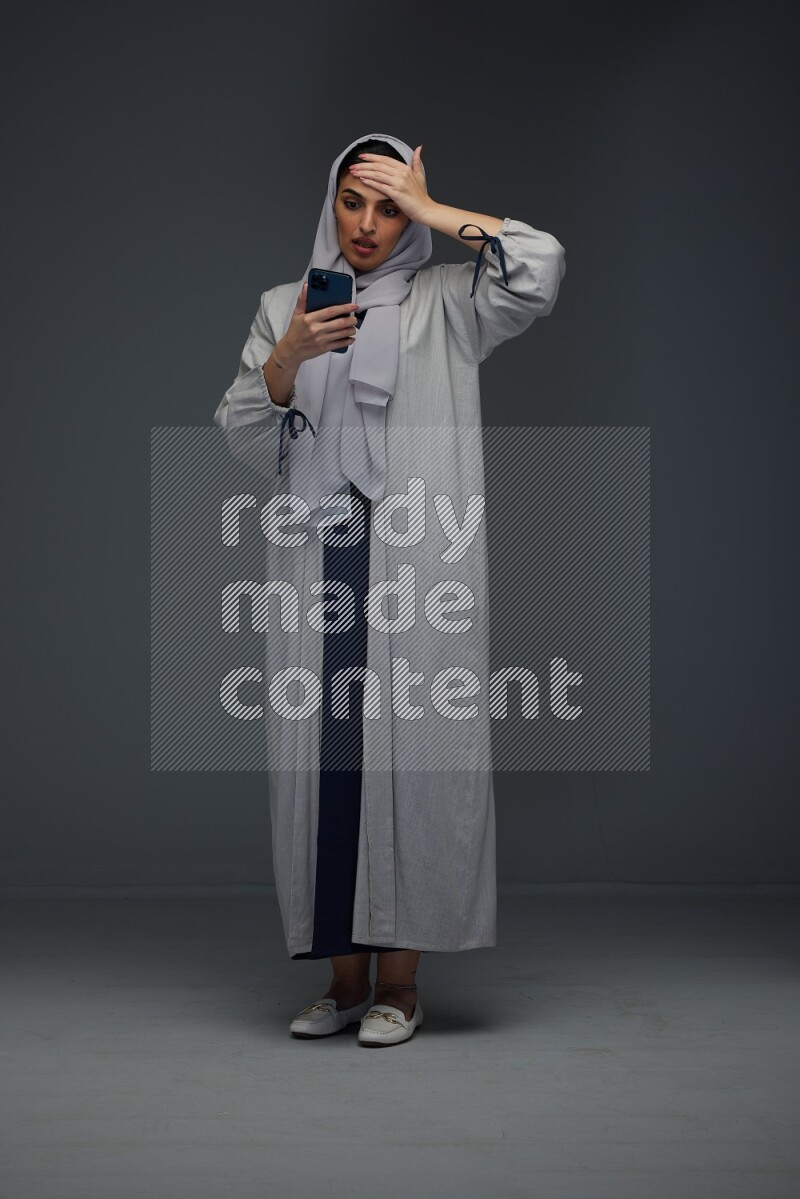 A Saudi woman wearing a light gray Abaya and head scarf standing and pointing in different directions eye level on a grey background