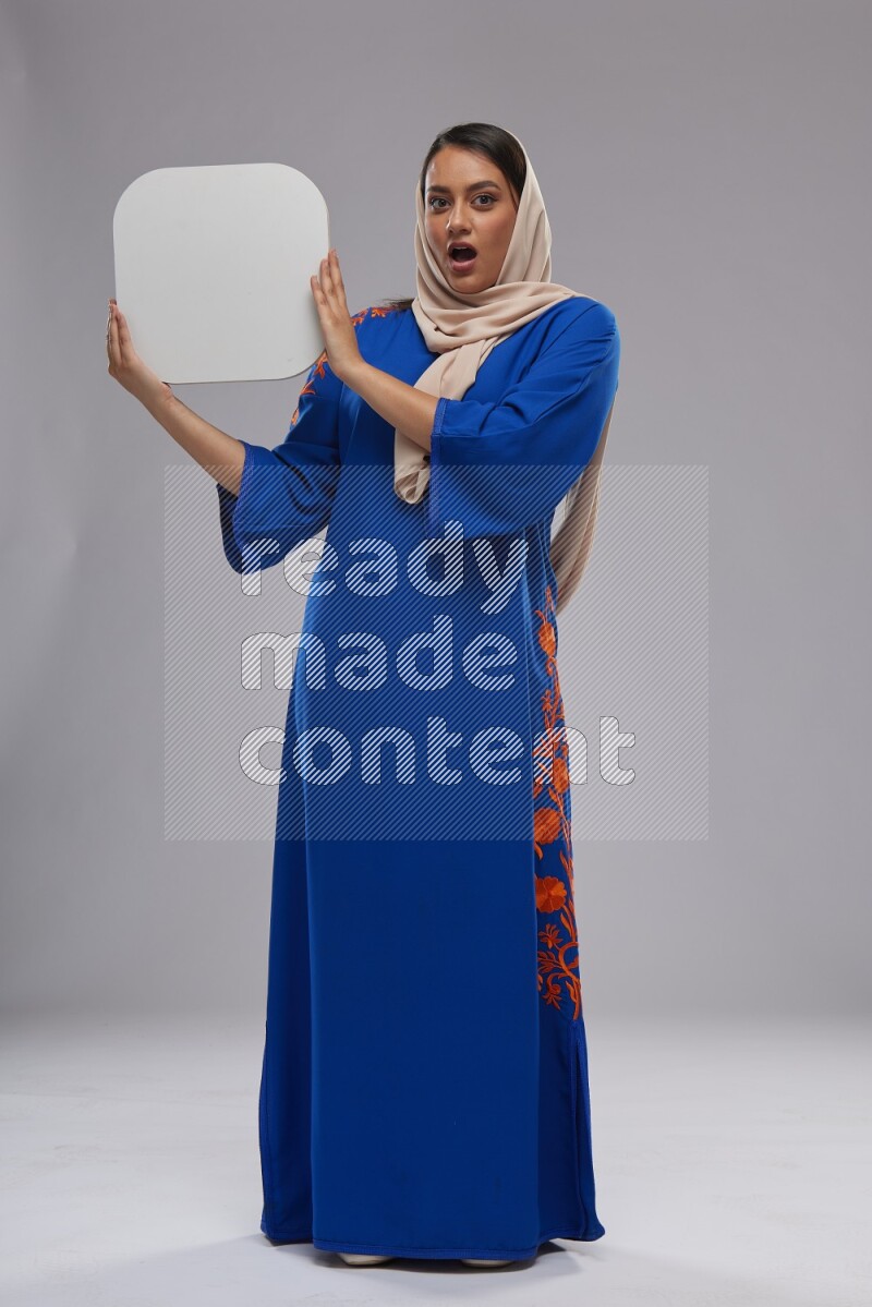 A Saudi woman standing wearing Jalabeya holding a social media sign
